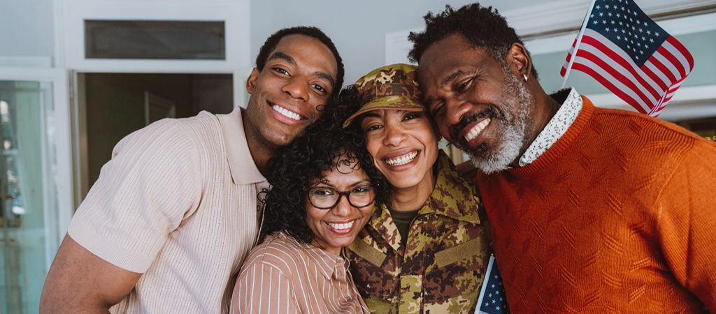 A female US veteran smiling with family around her, holding American flags.